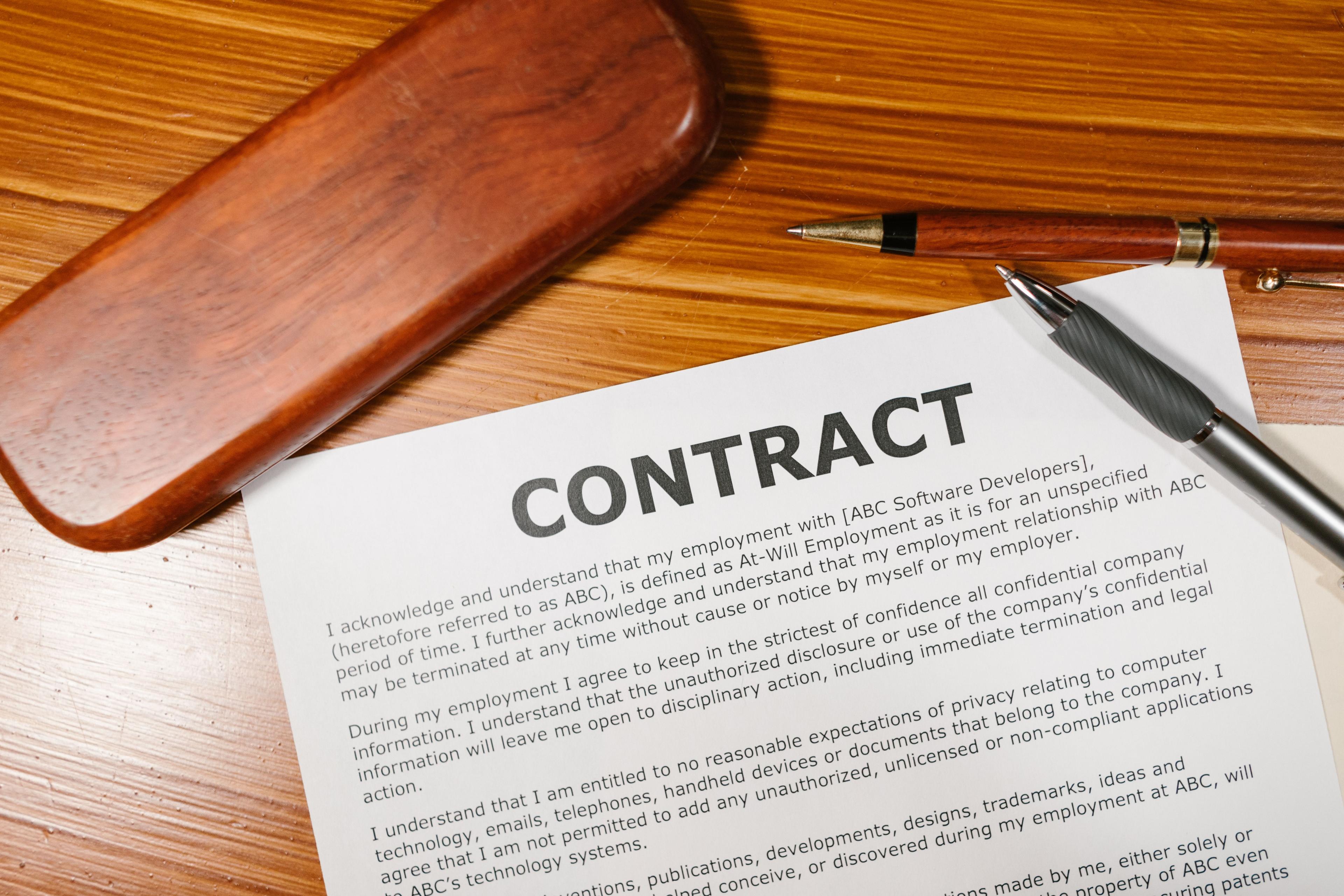 Documento contractual sobre una mesa de madera con bolígrafos